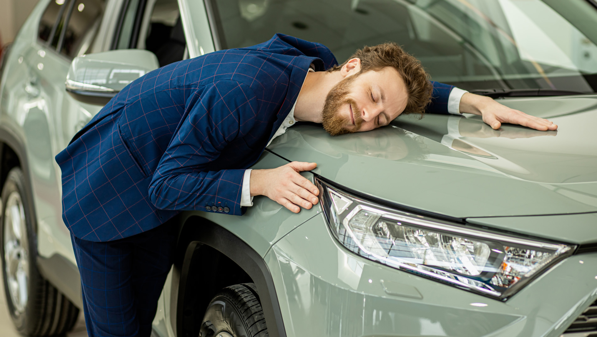 Hombre feliz abrazando el capó de su carro nuevo
